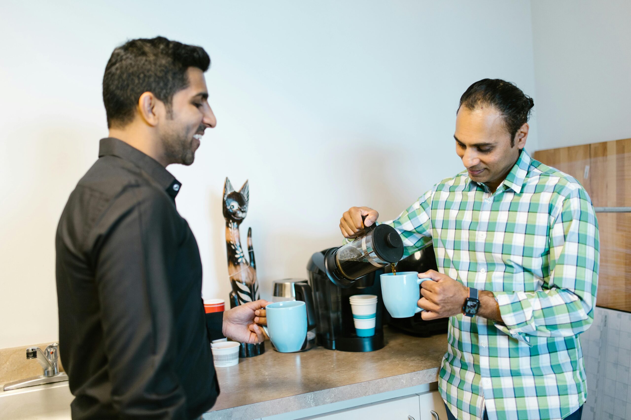 Two male colleagues enjoying a coffee break at the office, sharing a warm moment.